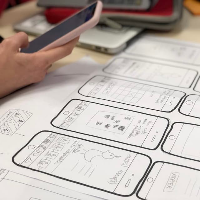 Paper mobile wireframes beside a phone being tested